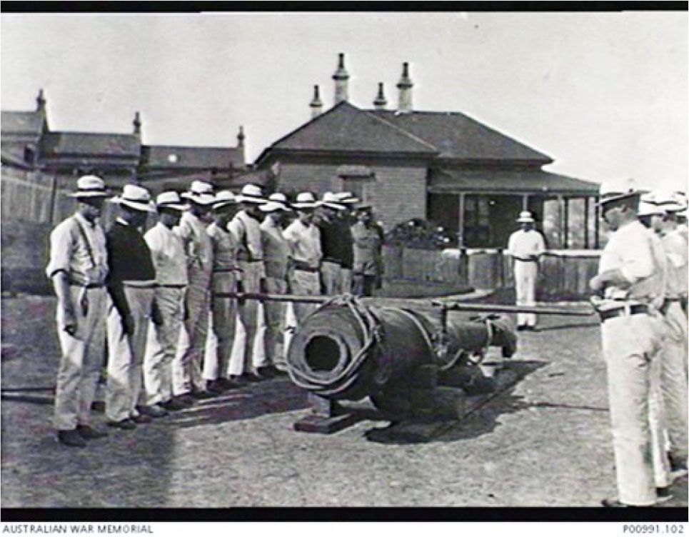 1910. Members of the Short Course (1910-04-24 to 1910-07-23) at the South Head Commonwealth School of Gunnery receiving instruction on moving a 6 inch, Mark 5 gun barrel. the Officers Mess is in the background. (Donor, Royal Australian Artillery Historical Society)
